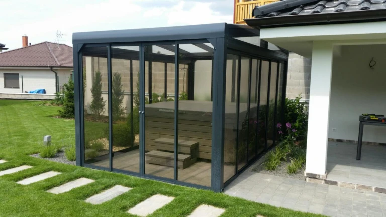 A modern glass-enclosed shelter with a hot tub located in the garden of a single-family home.