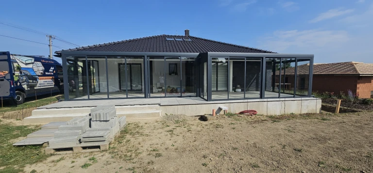 A modern glass-enclosed sunroom with an anthracite-colored frame attached to a single-family home
