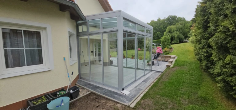 A modern, glass-enclosed sunroom with an aluminum frame attached to a single-family home