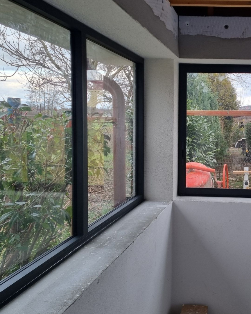 A close-up view of the corner glazing on the terrace, featuring dark aluminum frames and a view of the garden.