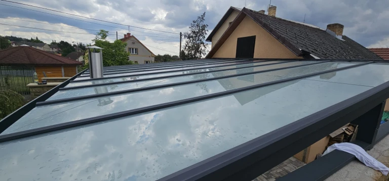 A bird's-eye view of the glass roof of a modern sunroom with a dark frame attached to a single-family home