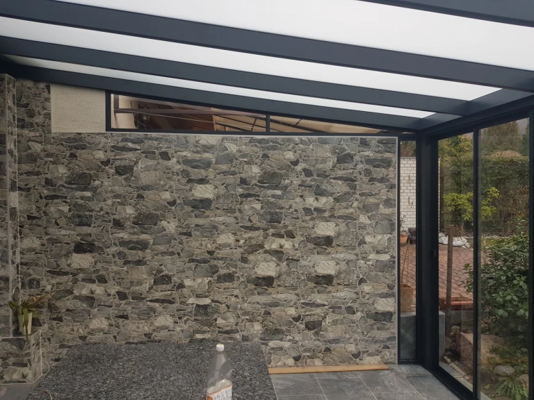 A modern sunroom with an anthracite-colored frame and stone wall cladding.