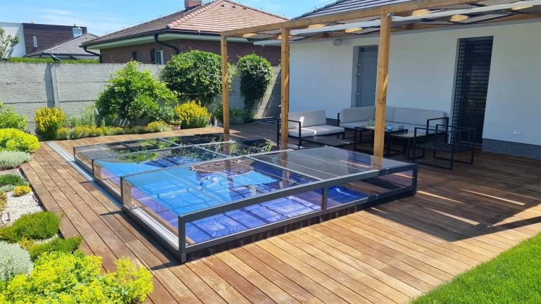 A modern, low-profile glass pool enclosure on the wooden deck of a single-family home