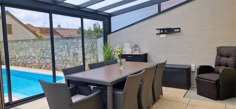 The furnished interior of the maintenance-free ROBUST conservatory, featuring a dining table and a view of the pool