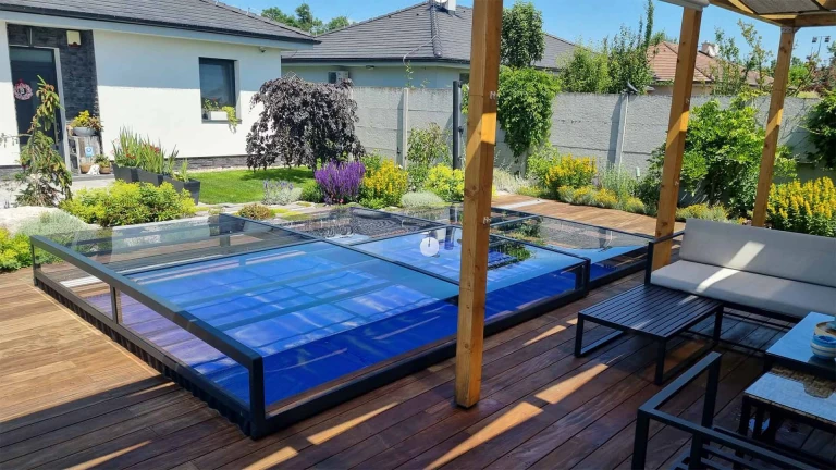 A modern, low-profile glass pool enclosure on a wooden deck next to a single-family home in the garden