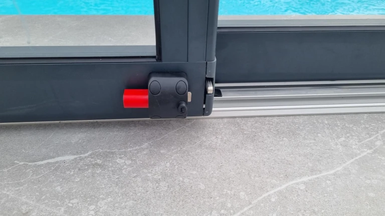 Close-up of the locking mechanism on an aluminum pool cover with a red safety latch
