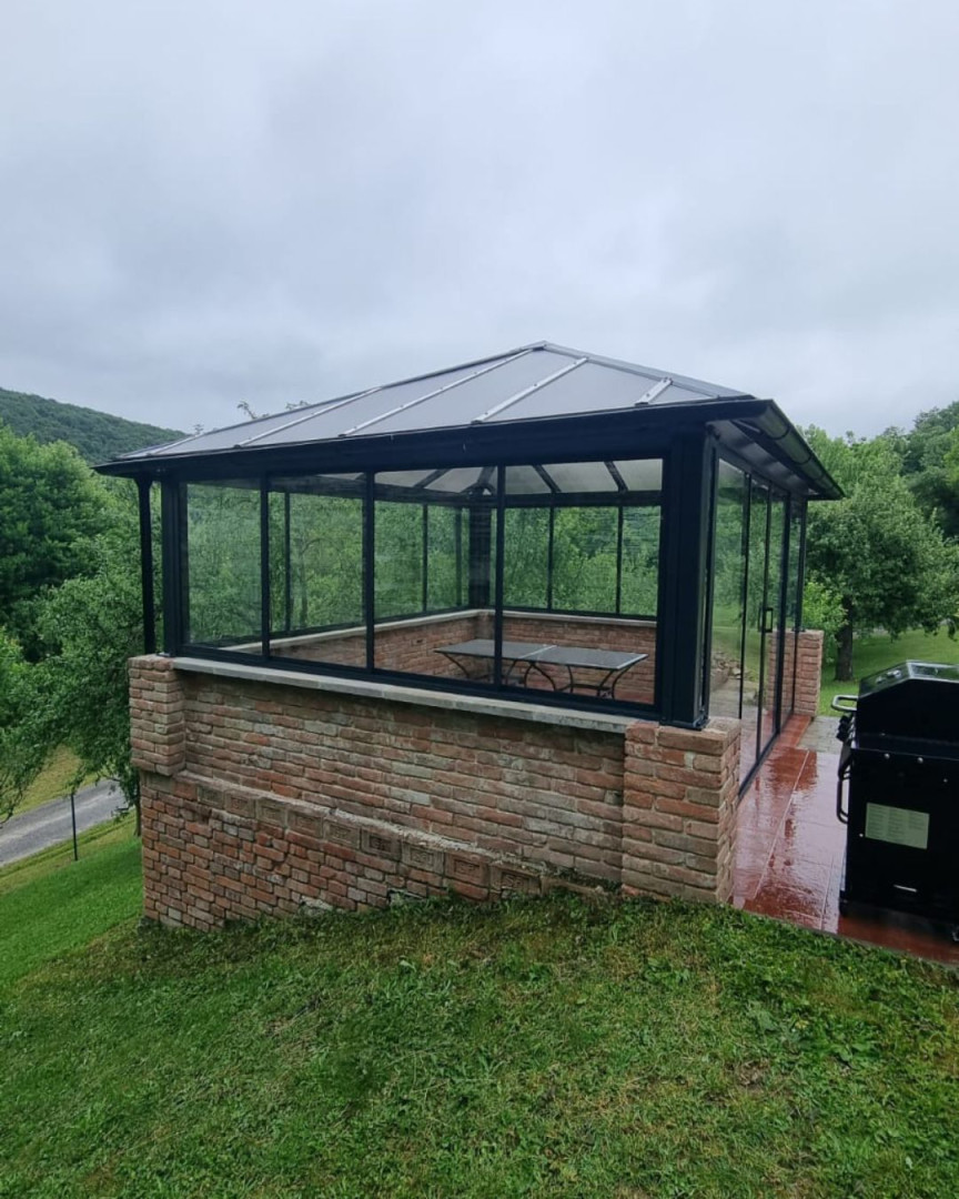 A modern glass gazebo with a brick foundation in the garden