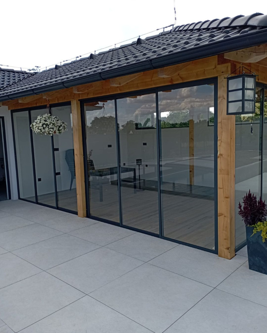 Modern terrace glazing with a sliding system in a wooden structure beneath a dark roof.