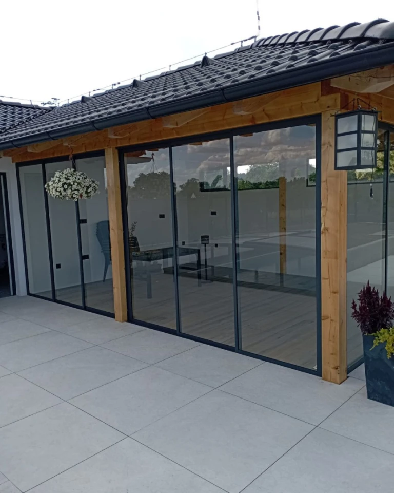 Modern terrace glazing with a sliding system in a wooden structure beneath a dark roof.