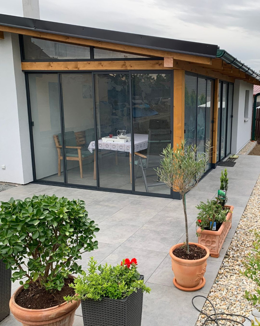 Modern terrace glazing with a sliding system and a wooden frame at a single-family home, with flower pots in the foreground.