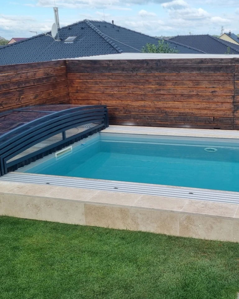 A modern, low-profile pool enclosure in a dark color with a view of the backyard