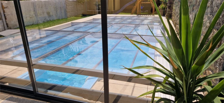 A modern, low-profile pool enclosure with translucent panels in the garden