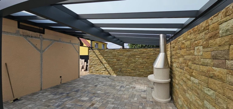 A view of the terrace with a dark gray aluminum structure and an outdoor fireplace set against a stone backdrop