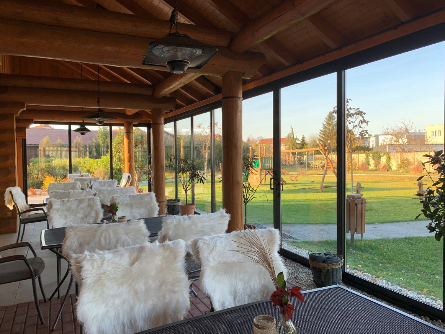 A glass-enclosed terrace in a log cabin with a view of the garden and the playground