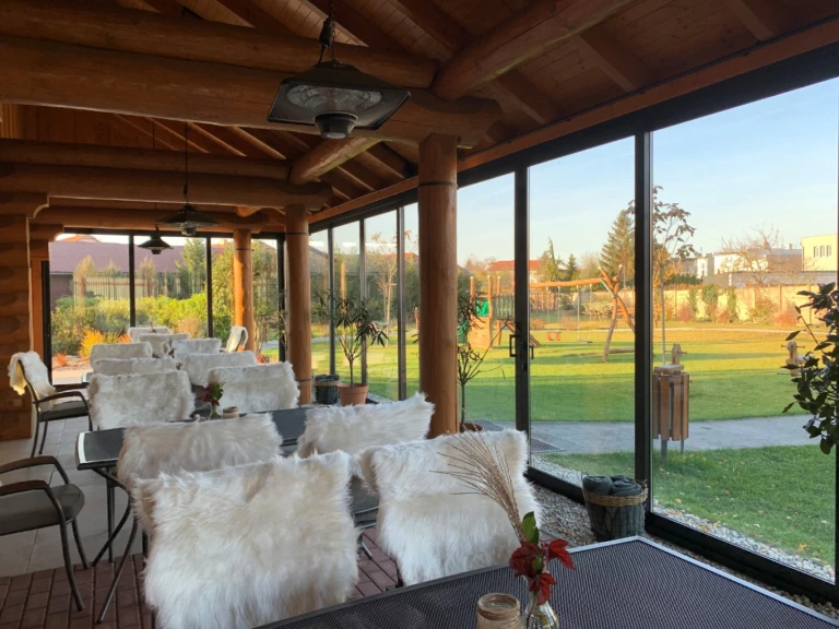 A glass-enclosed terrace in a log cabin with a view of the garden and the playground