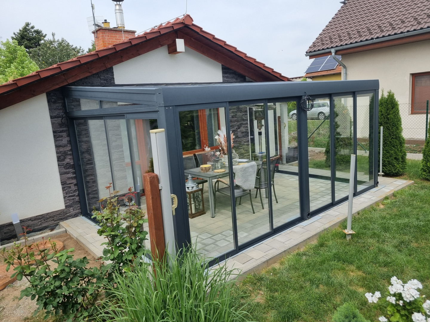 A modern glass-enclosed sunroom with an anthracite frame and sliding doors attached to a single-family home