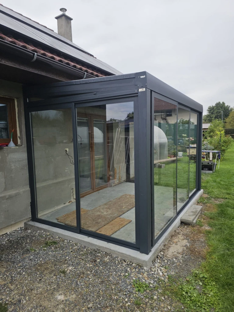A modern, glass-enclosed conservatory addition with a dark gray frame attached to a single-family home