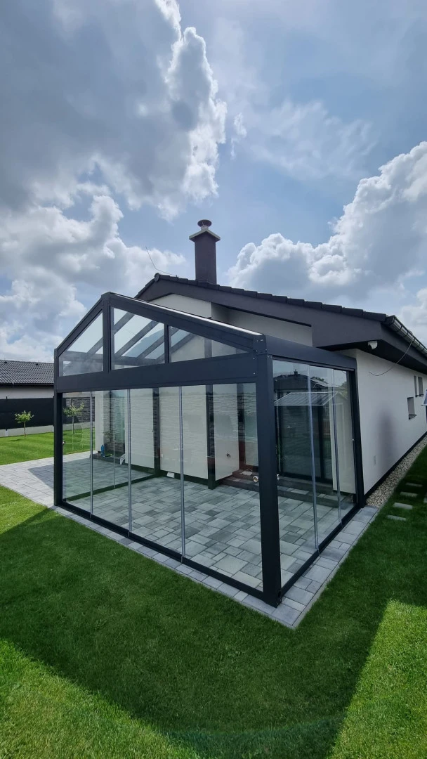 A modern, glass-enclosed sunroom with an anthracite-colored frame attached to a single-family home