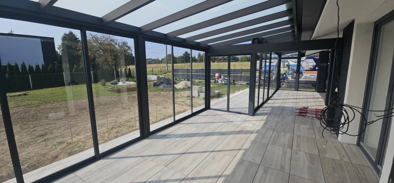 A modern glass-enclosed sunroom with an anthracite-colored frame and a view of the outdoors