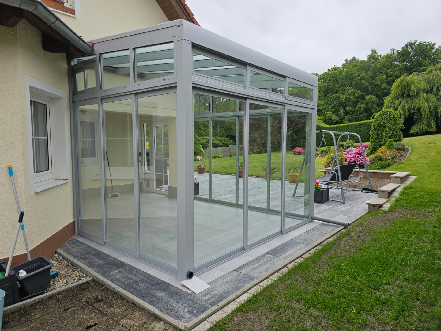 A modern, glass-enclosed sunroom with an aluminum frame attached to a single-family home