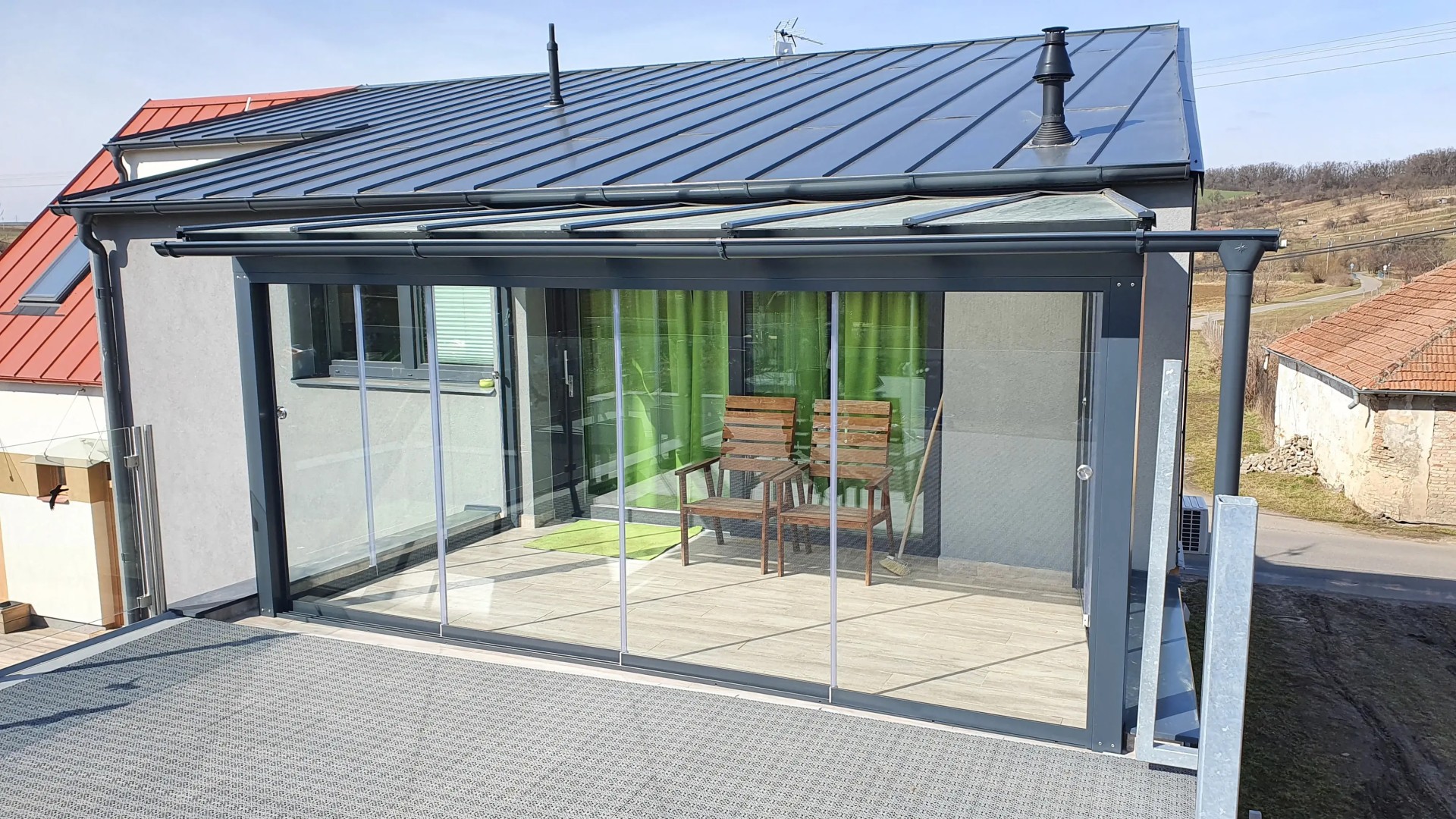 A modern glass-enclosed sunroom with an anthracite-colored frame and sliding glass doors on the house's terrace.