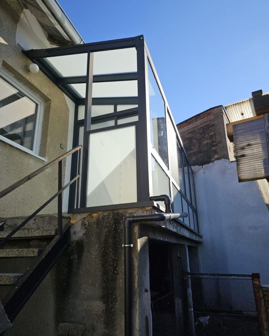 A modern, glass-enclosed Robust sunroom with a dark frame, attached to the wall of the house.